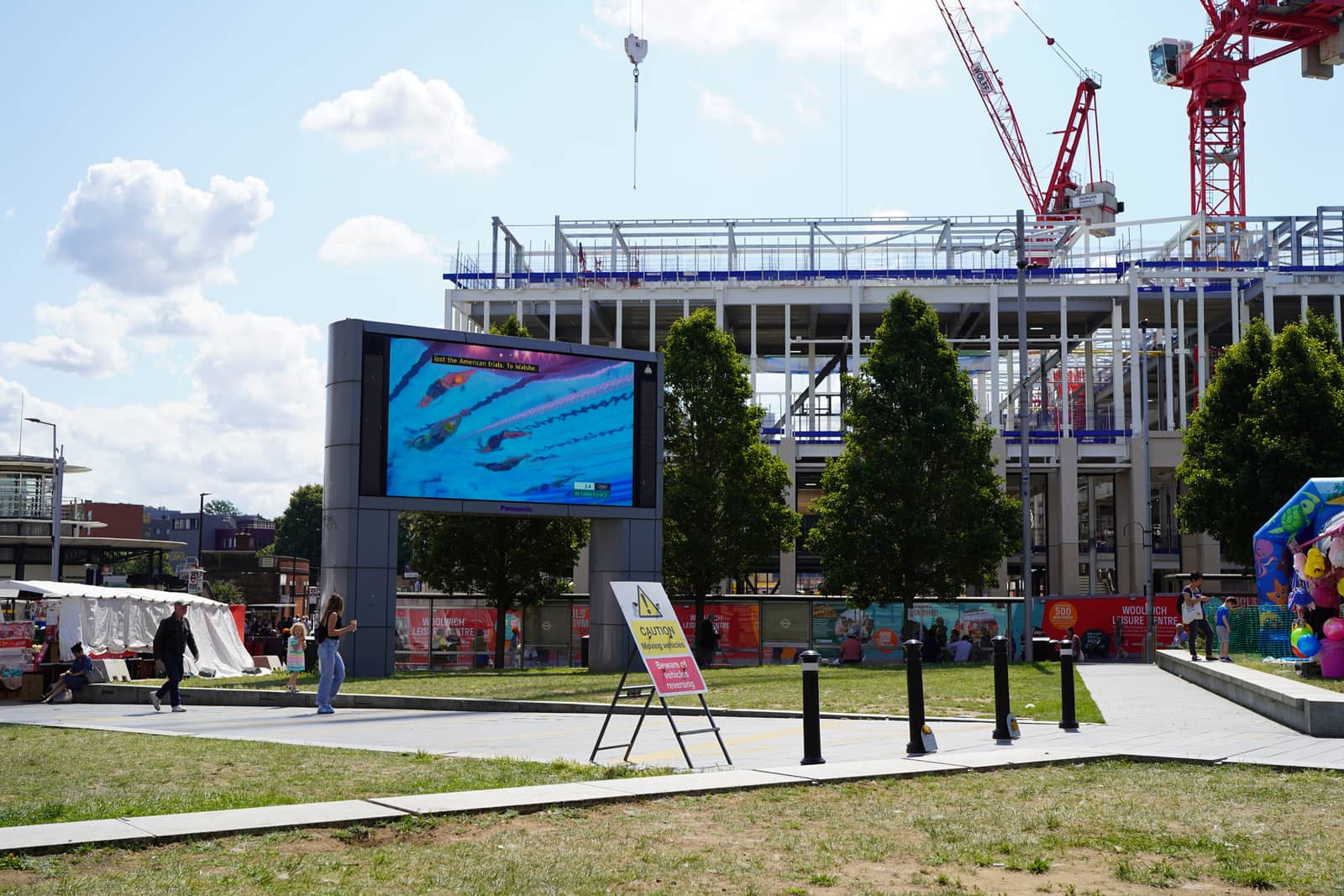 A big public screen and bouncy castle in a park, construction cranes behind