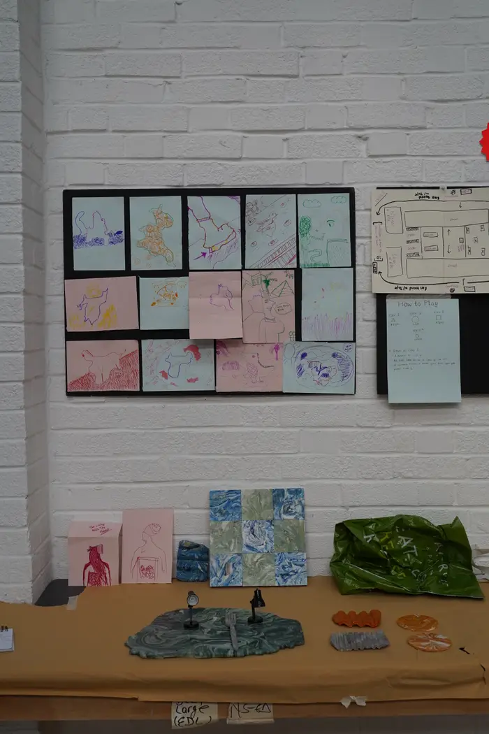 A wall of drawings pinned above a table of models