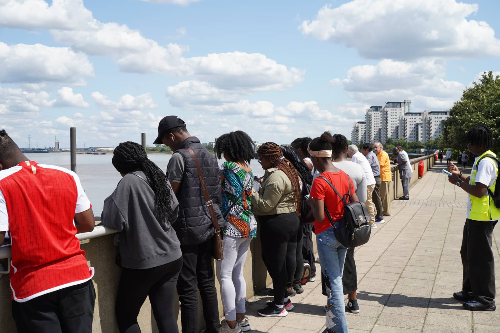 A group of young people leaning on the riverside railing, looking out over the Thames