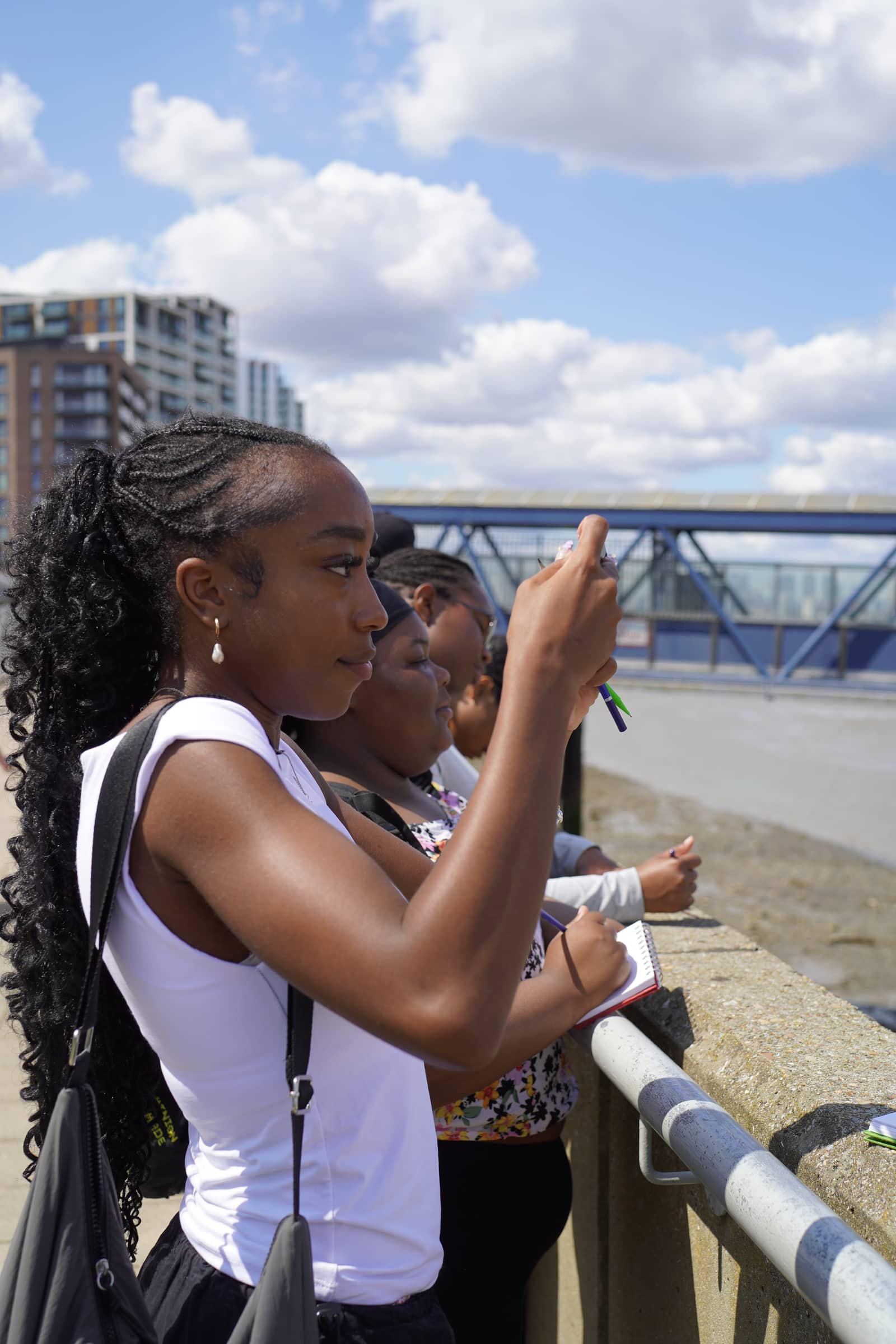 A young woman photographing the river from the path, others sketching beside her