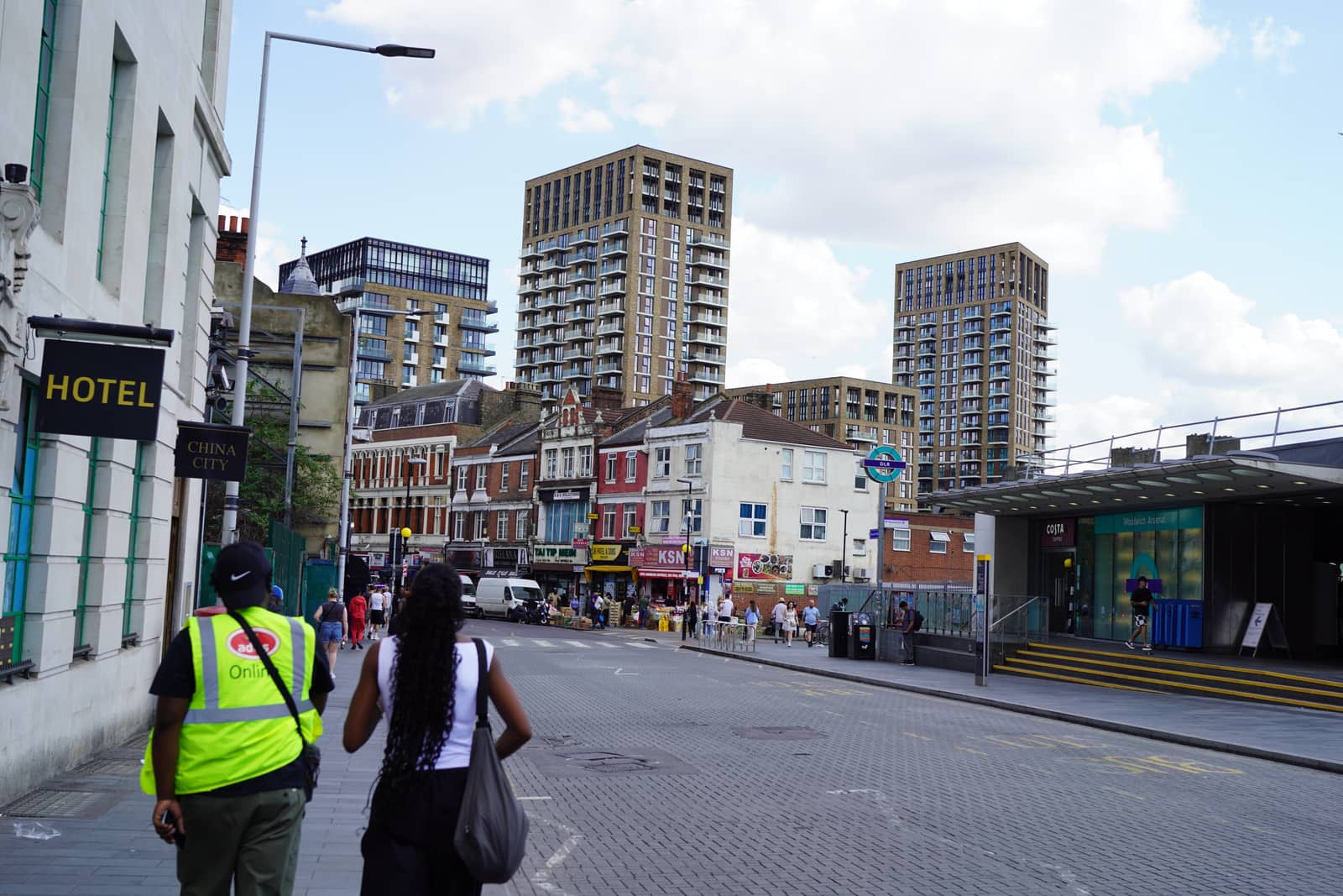 Two people walking up a high street, new towers rising behind the old shopfronts